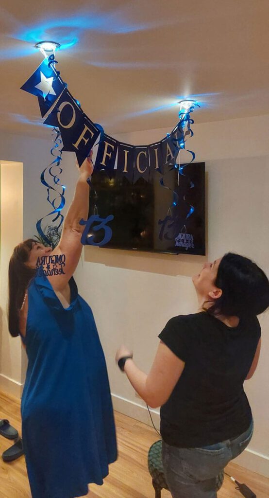 Two women hanging a banner in front of a television.